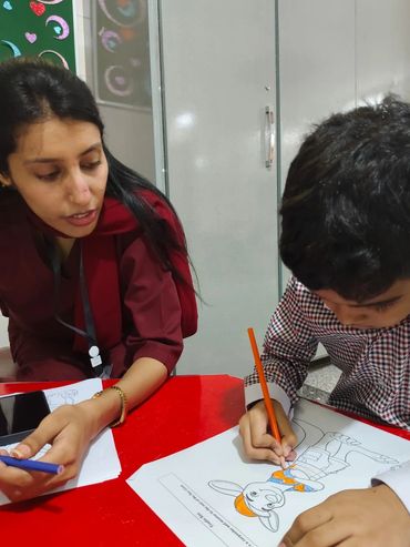 A woman helping a child color a cartoon drawing at a red table.