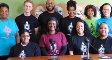A group of diverse people posing for a photo with microphones in front.