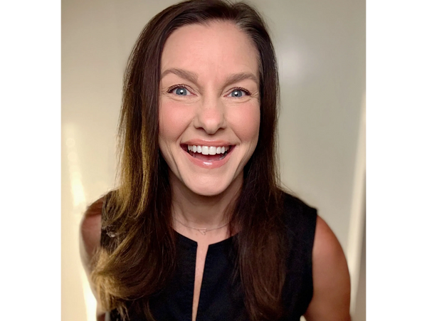 Smiling woman with long brown hair wearing a black sleeveless top.
