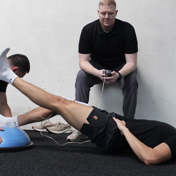 A man exercises with trainers monitoring and timing him.