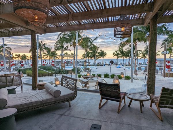 Resort patio overlooking a pool and palm trees at sunset.