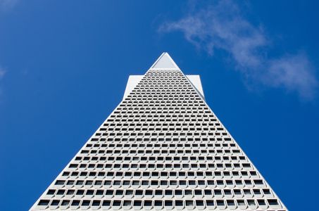 Upward view of a triangular-patterned skyscraper against a clear blue sky.