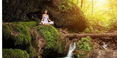 A woman meditating on a mossy creek side