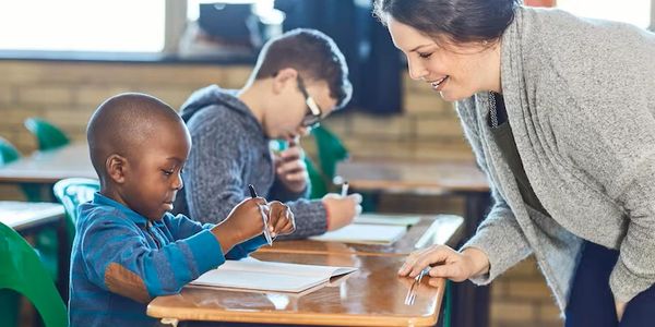 Teacher helping young student with writing in classroom.