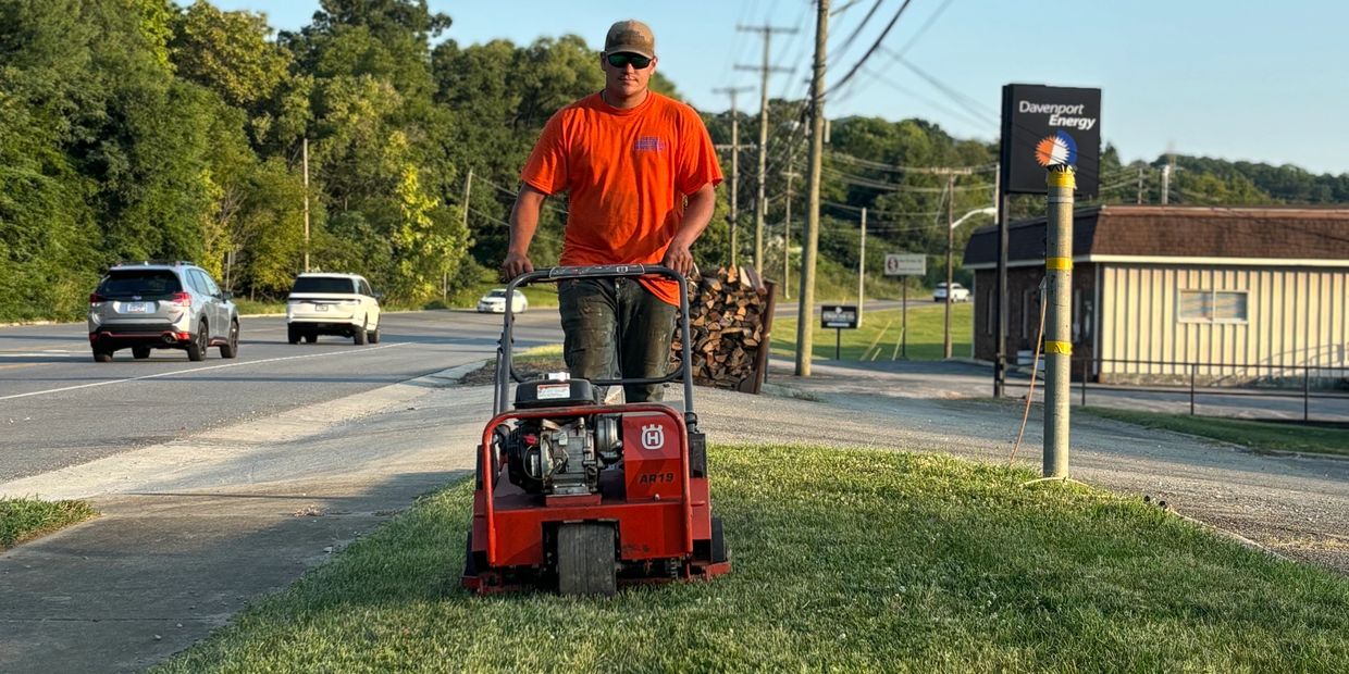 Man core aerating grass near a road.