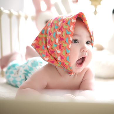 Baby in colorful head scarf happily crawling on a bed, refreshed from a nap and restful sleep.
