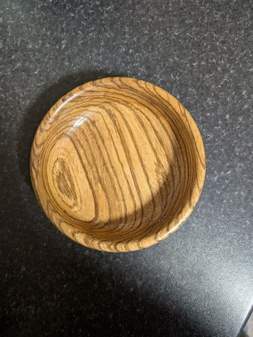 Round wooden bowl with natural grain on dark countertop.