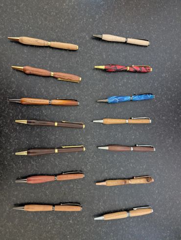 Collection of handcrafted wooden and resin pens on a dark surface.