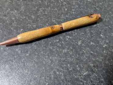 Handcrafted wooden pen with copper accents on a dark surface.