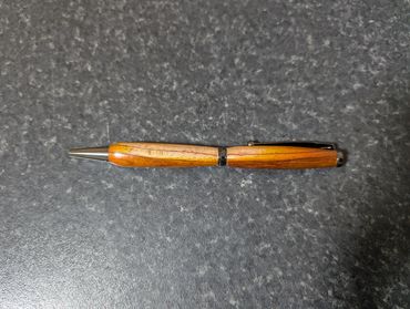 Wooden pen with metallic tip and clip on a textured surface.