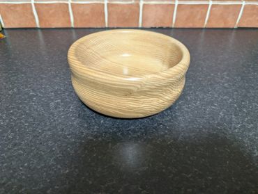 A smooth, polished wooden bowl on a dark countertop with a tiled backsplash.