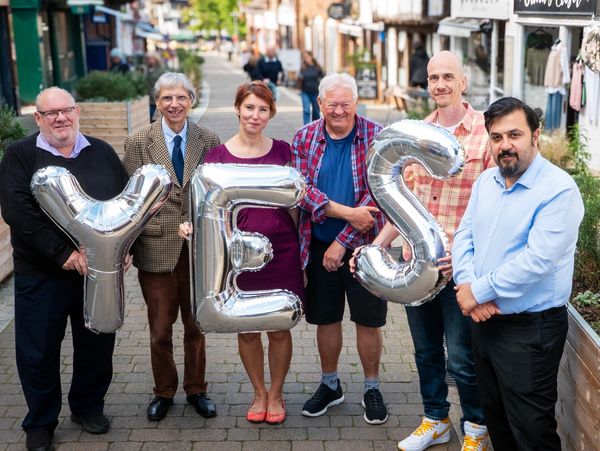 Group of six people holding silver balloons spelling 'YES' in a street.