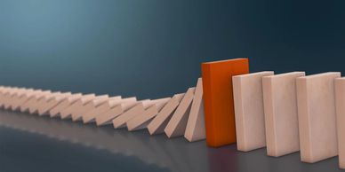 A single orange domino stopping a falling line of beige dominoes.
