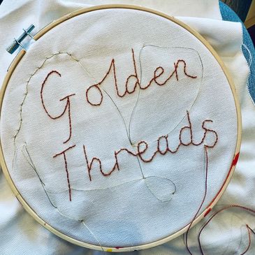 Embroidery hoop with the stitched words 'Golden Threads'.