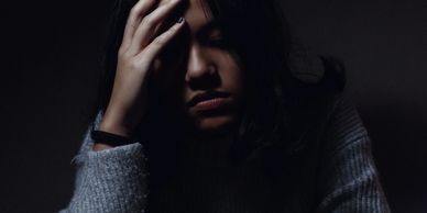 Girl looking sad with her head in her hands against a dark background