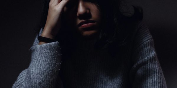 Girl looking sad with her head in her hands against a dark background