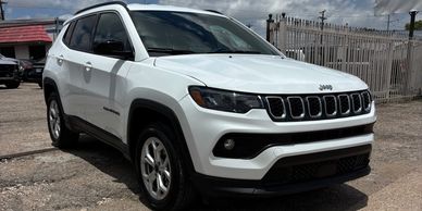 White Jeep Compass parked on a rough street under a cloudy sky.