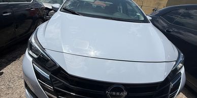 Front view of a white Nissan car parked between two black vehicles.