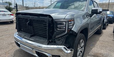 Gray pickup truck with front-end damage and missing grille in a parking lot.