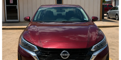 Red Nissan sedan parked in front of a building.