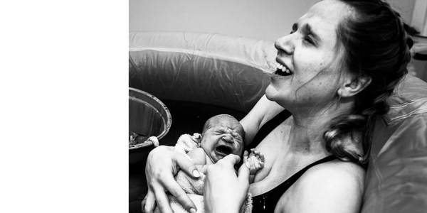 Happy mother holding newborn after a waterbirth at home with a midwife
