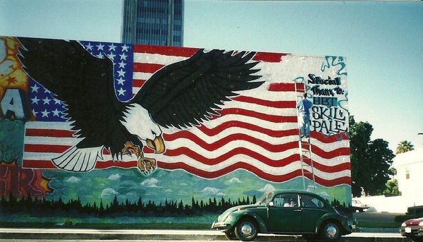A mural of an eagle and American flag with a vintage car parked nearby.