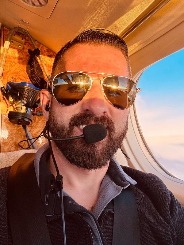 Pilot wearing sunglasses and headset inside an aircraft cockpit.