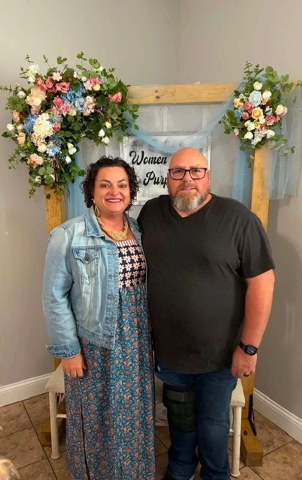 A couple posing happily in front of a floral decorated wooden frame.