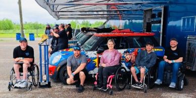 Group of people with disabilities posing by race cars.