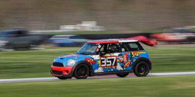 Racing Mini Cooper with superhero-themed livery speeds on track.