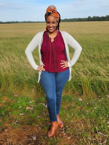 Woman standing confidently in a field, smiling at the camera.