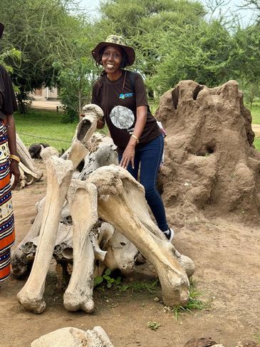 Woman posing with large animal bones outdoors near termite mound.