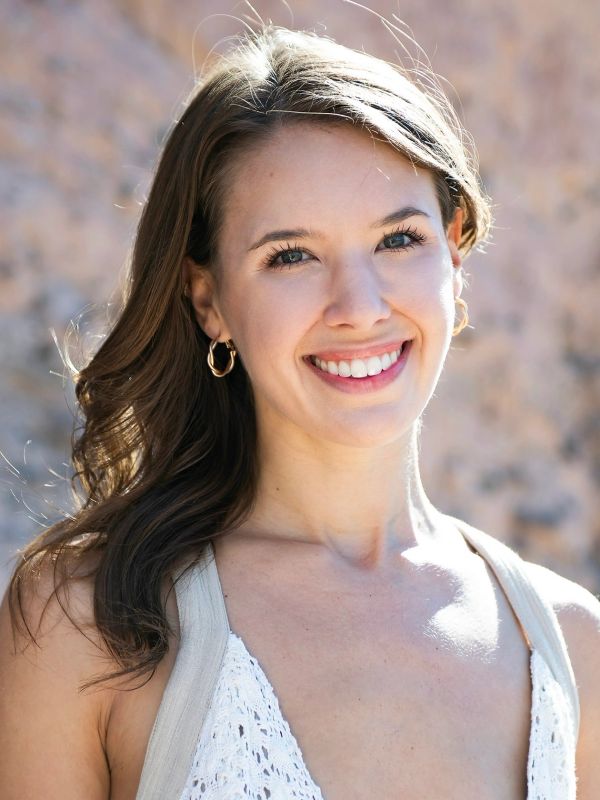 Smiling woman with long brown hair and gold hoop earrings.