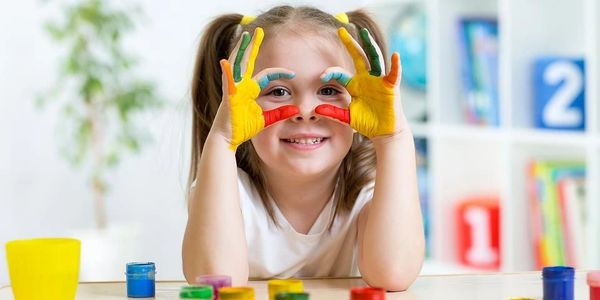Smiling girl with colorful painted hands making binoculars.