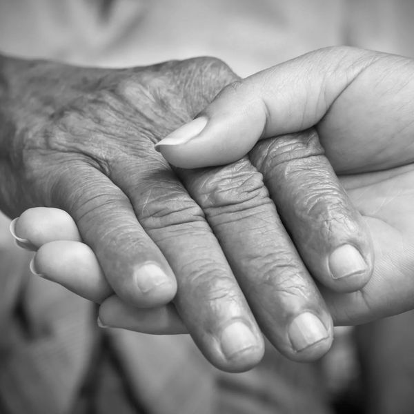 A younger hand gently holding an elderly hand, symbolizing care and support.