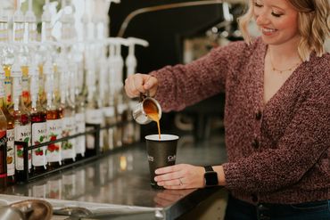 Barista pouring coffee into a paper cup at a coffee shop.