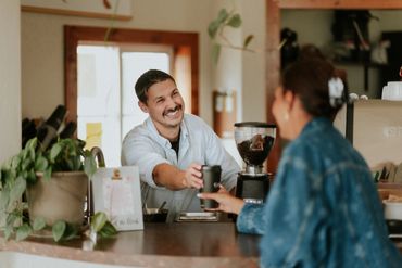 Barista smiling while handing a coffee cup to a customer.