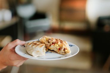 Hand holding a plate with a sliced stuffed pita bread sandwich.