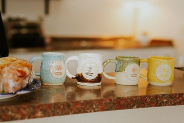 Four colorful ceramic mugs lined up on a kitchen counter near pastries.