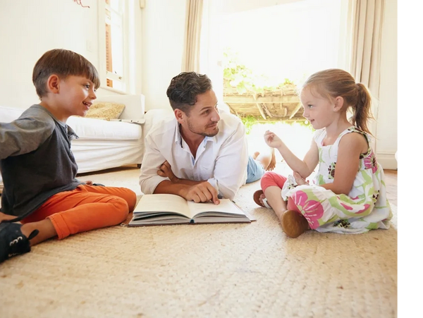 father and children sitting on floor reading together