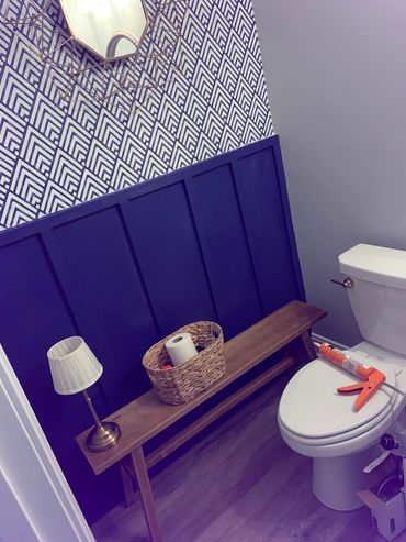 A stylish bathroom corner with blue paneled wall, wooden bench, and decorative mirror.