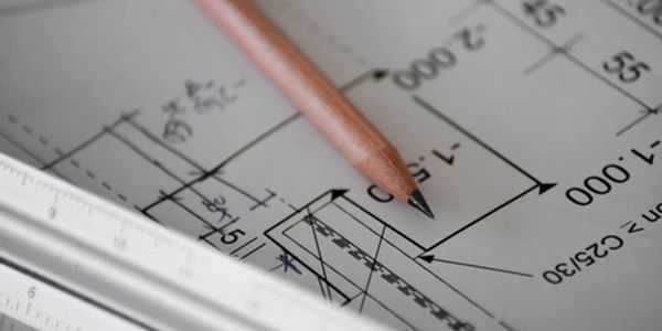 A pencil rests on an architectural blueprint with measurements and a ruler.
