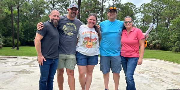 Five friends smiling together outdoors in casual attire.