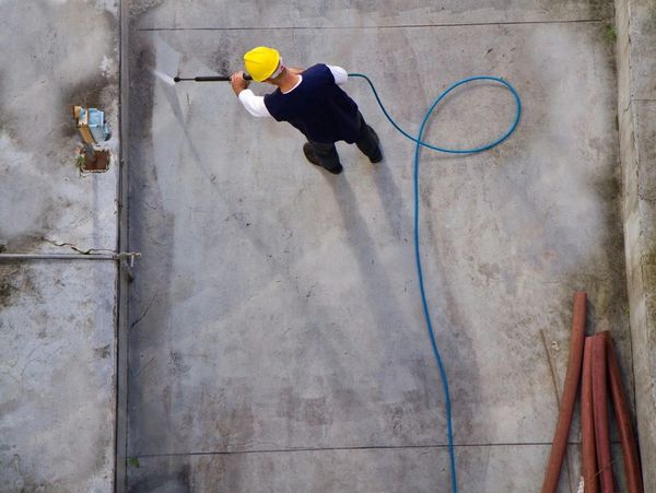 A shot of a man pressure washing concrete.