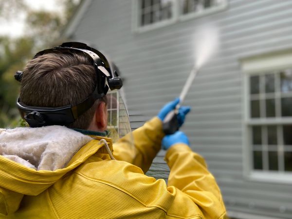 A shot of a man pressure washing vinyl siding.