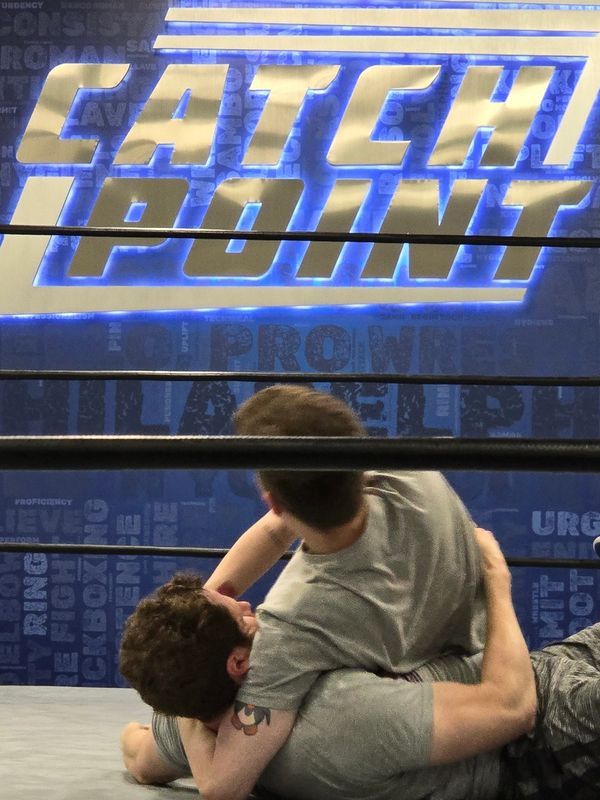 Two wrestlers engaged in a headlock on the canvass of the ring at Catchpoint Philadelphia.