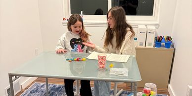 Two girls engaged in a creative activity at a table indoors.