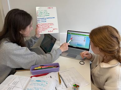 Two students collaborating on a laptop with notes and stationery nearby.