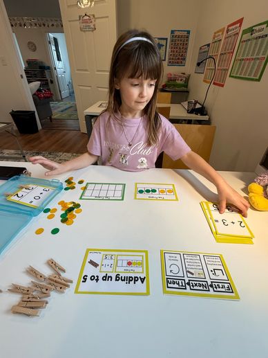 A young girl learning addition with cards and counters at a table.