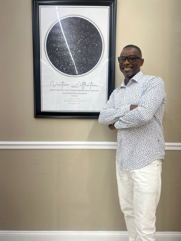 Man smiling with arms crossed standing next to a framed star map on the wall.